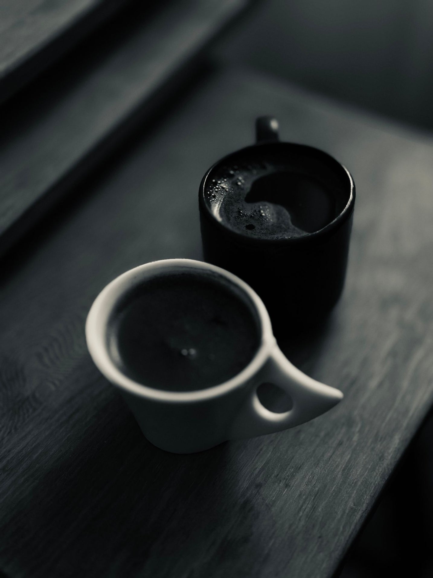 Two coffee cups side by side on a dark wooden table