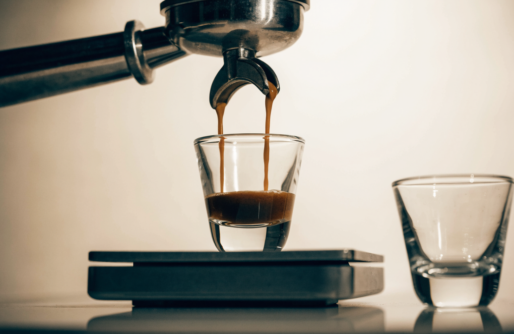 Portafilter pouring espresso into a shot glass on a scale, illustrating weighing an espresso ratio