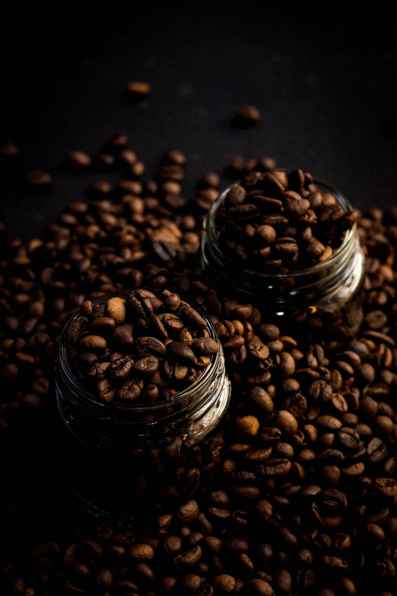 Glass jars overflowing with dark roasted coffee beans