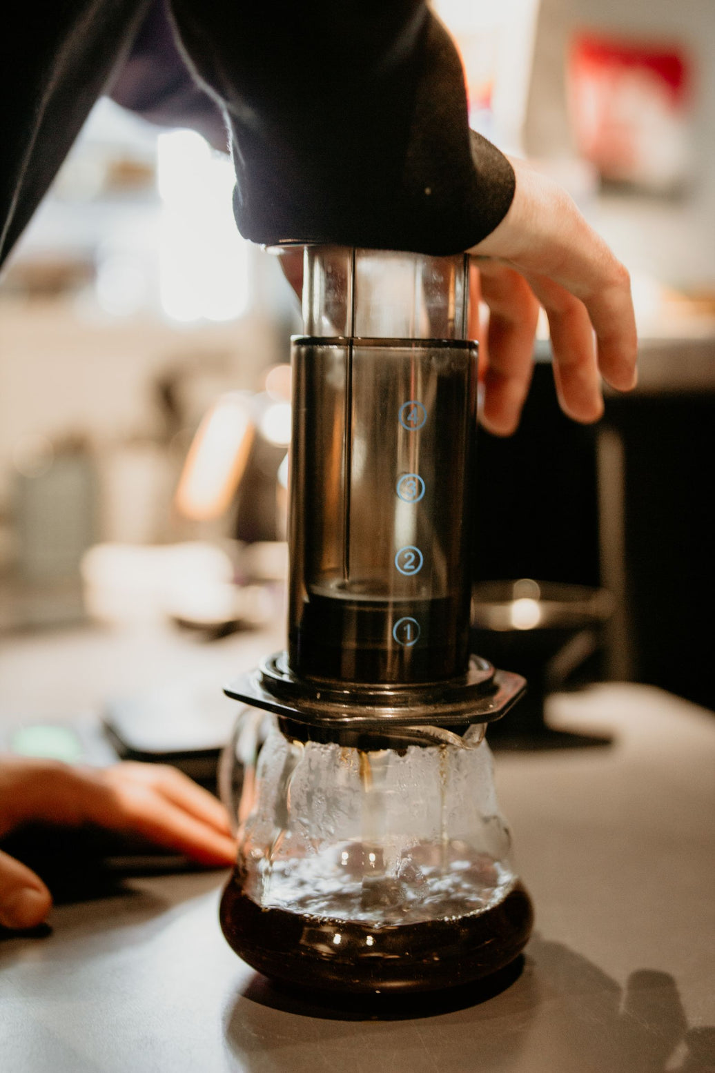 Hands pressing an AeroPress to brew coffee into a glass carafe