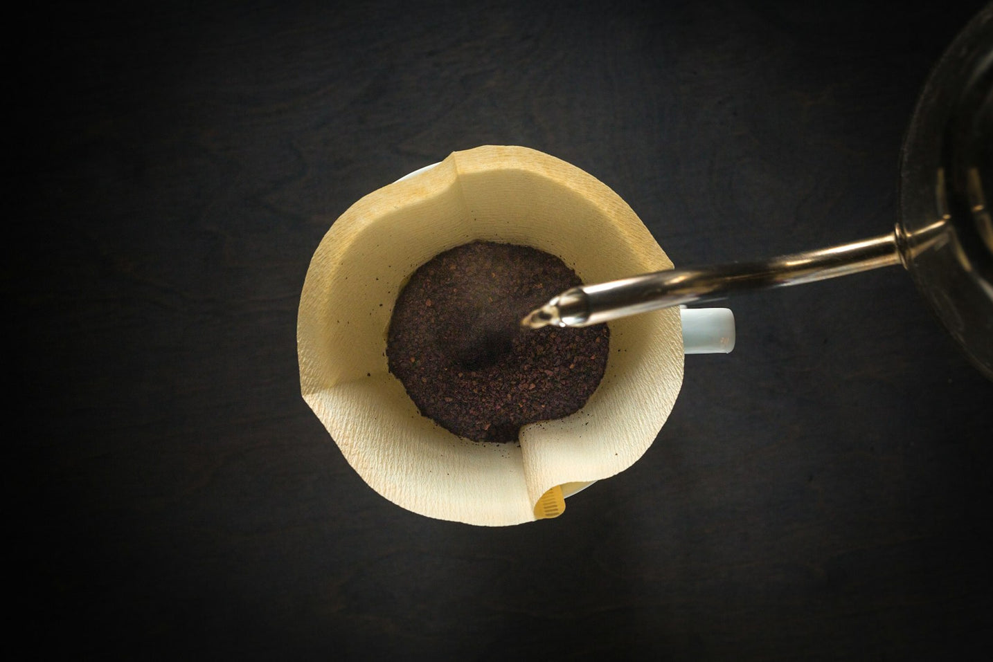 Hot water poured in a slow spiral over a pour-over coffee brewer, seen from above