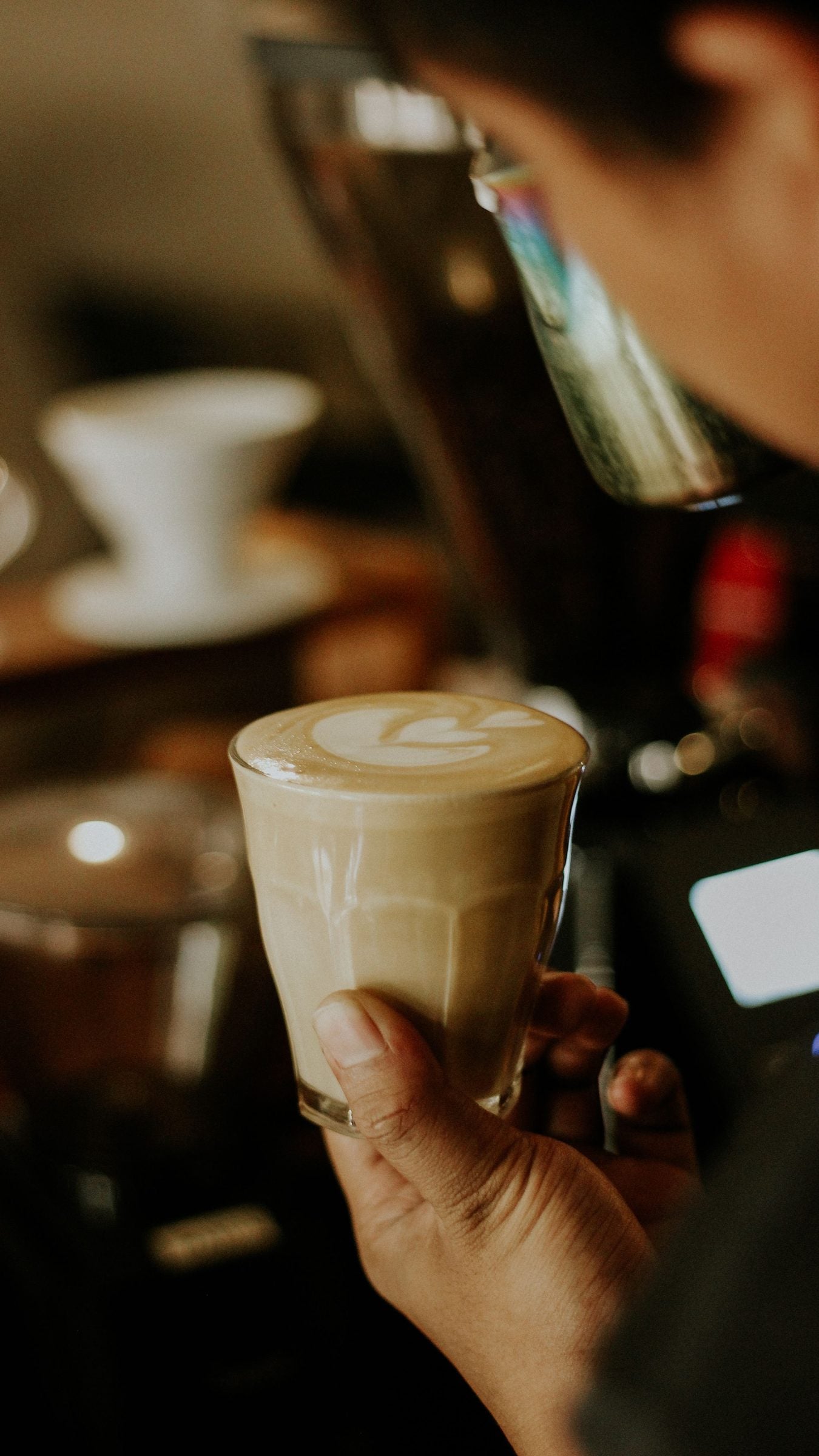 Hand holding a latte topped with foam in a glass at a cafe bar
