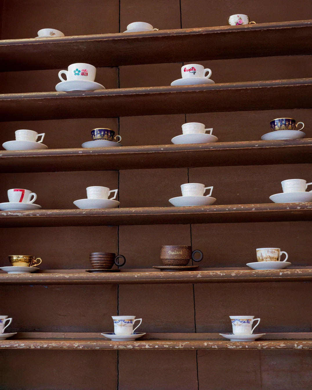 Collection of coffee cups arranged on warm wooden shelves