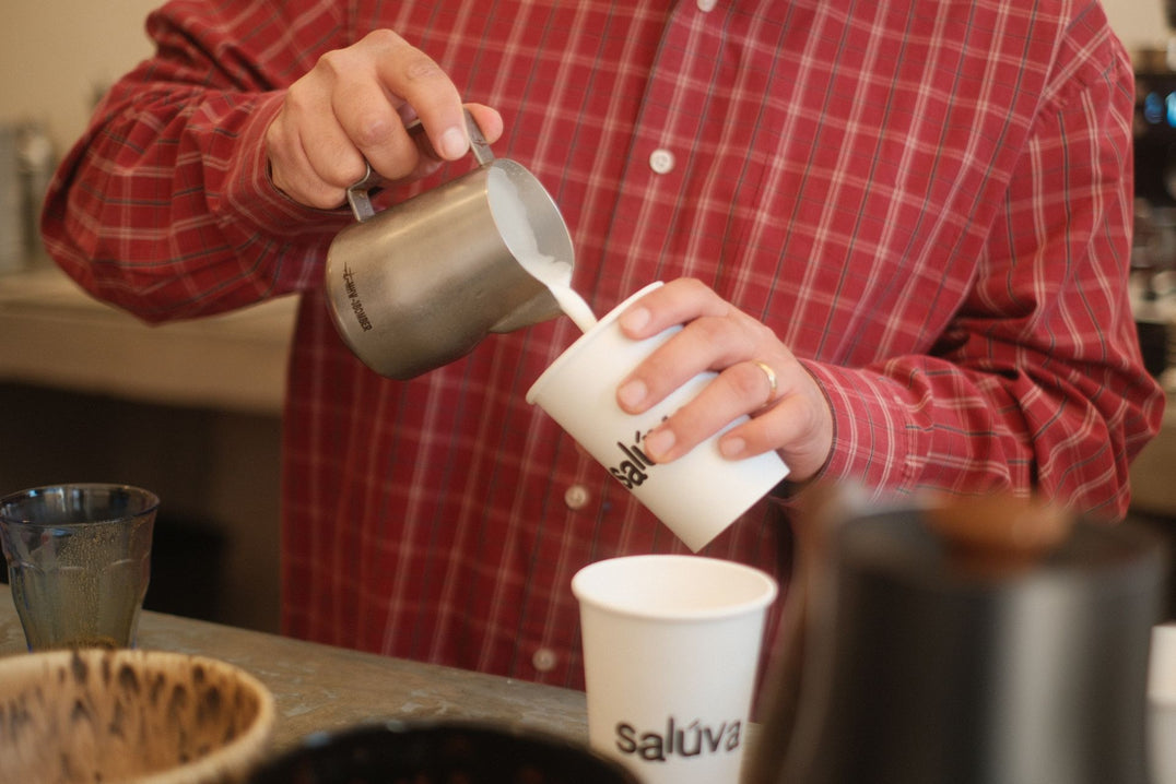 Barista pouring steamed milk from a pitcher into a coffee cup